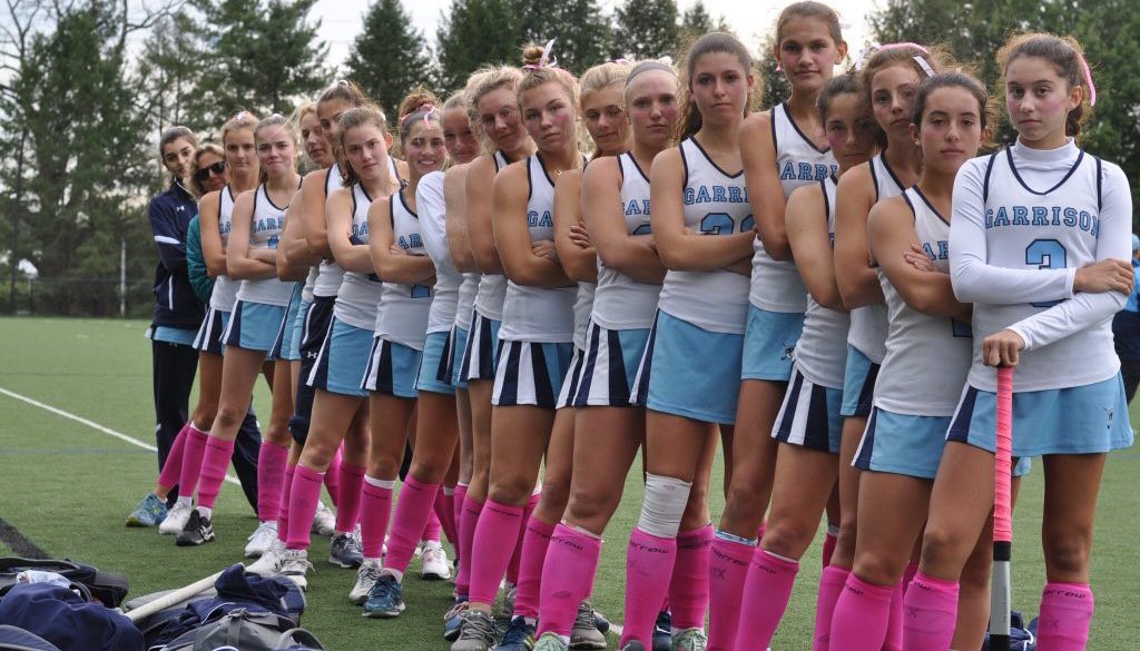 Garrison Forset Field Hockey wear pink socks for their Play4TheCure game High School Field Hockey Team stands in a line with pink socks for breast cancer awareness