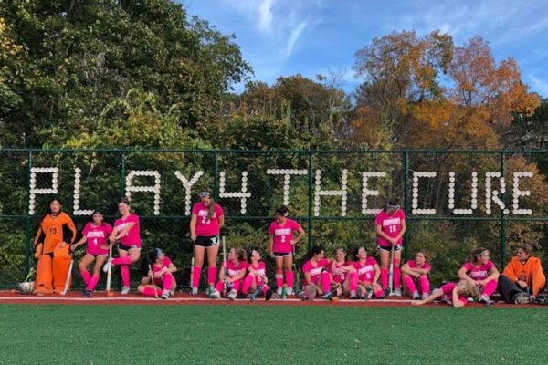 The Gunnery School Field Hockey pose in pink in front of the fence they put cups in to spell out Play4TheCure