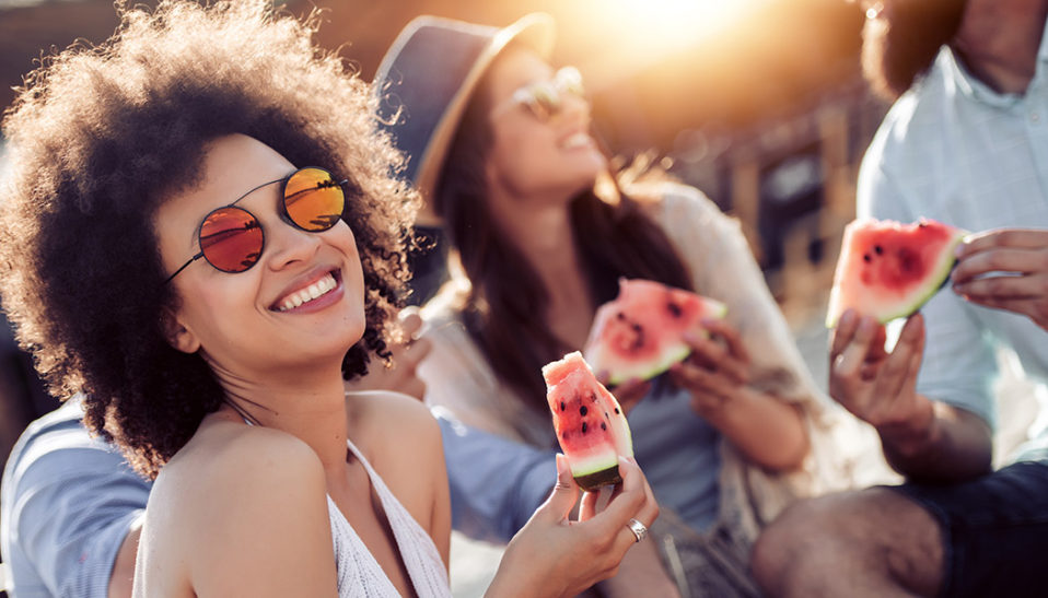Cheerful young friends eating watermelon on beach,having fun together.